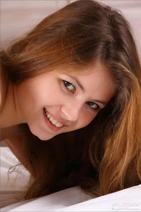 Очень симпатичная рыжеволосая девушка растягивается голышом на своей кровати, чтобы показать свою голую киску