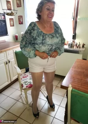 Пожилая женщина Каро стягивает свои колготки на высоких каблуках за кухонным столом