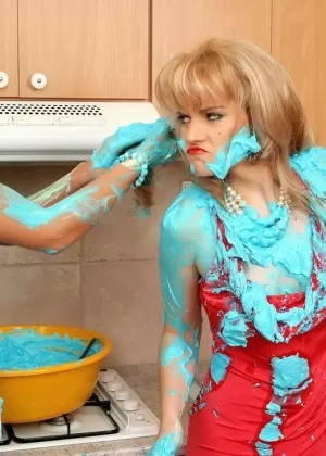 Clothed women cover each other in cake mix during a food fight in kitchen
