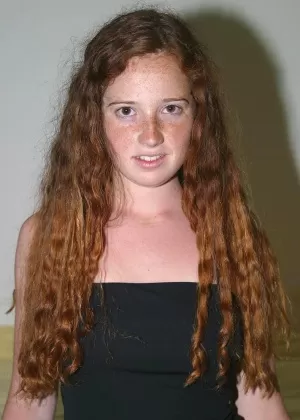 Молодая девушка с вьющимися рыжими волосами полностью раздевается на своей кровати